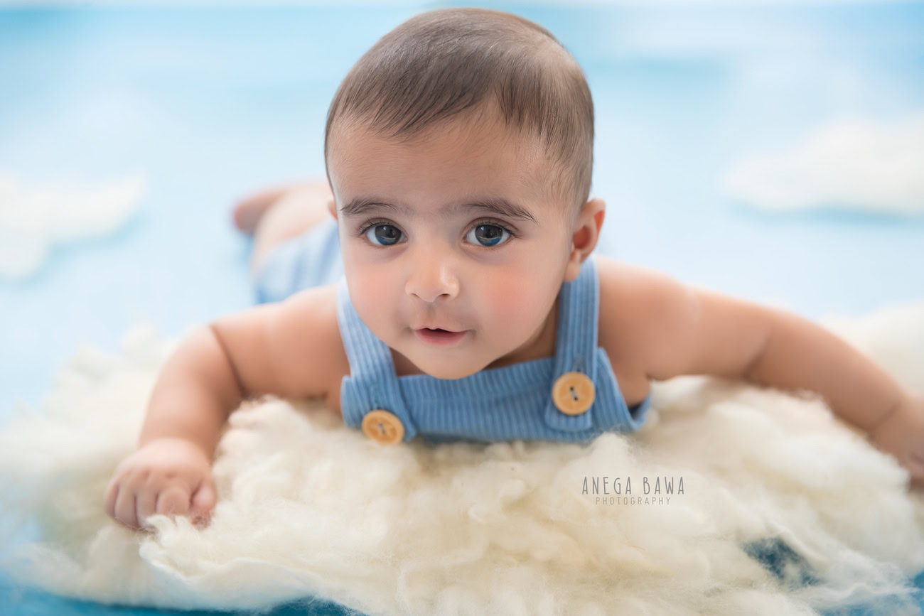 Captivating baby boy photography session featuring an adorable 5, 4, 3, 6-month-old on a soft white rug against a backdrop reminiscent of clouds. Crafted with expertise by Anega Bawa, the premier baby photographer in Delhi, Gurgaon, and Noida.