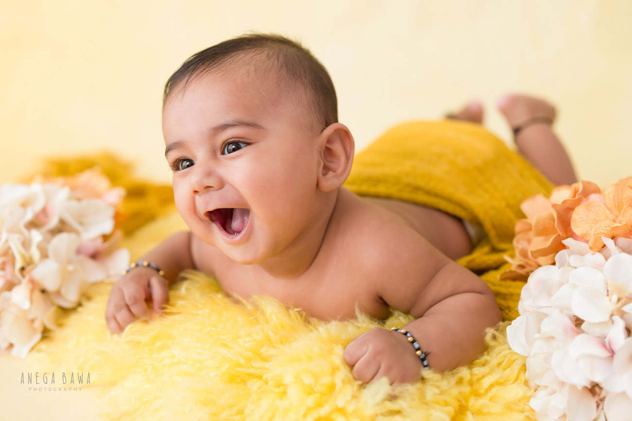 Baby boy photography, 5 or 4 or 3 or 6 months, yellow rug, white flowers, cute laughing pose. Location: Delhi, Gurgaon, Noida. Photographer: Anega Bawa.