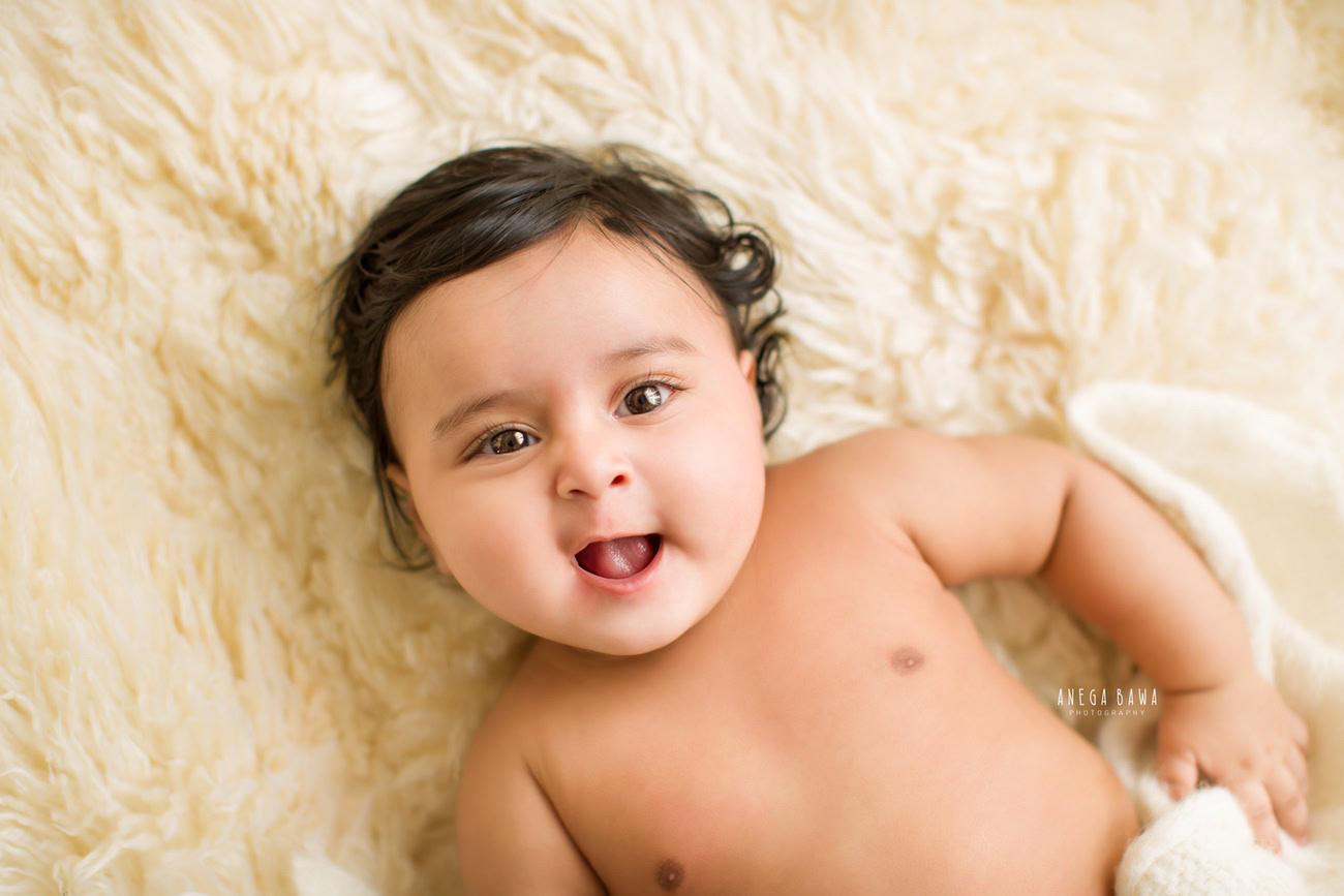 Captivating baby boy photoshoot capturing the mischievous charm of a 6, 5, 4, 3-month-old on a cozy beige rug against a complementary beige backdrop. Expertly crafted by Anega Bawa, your esteemed baby photographer in Delhi, Gurgaon, and Noida.