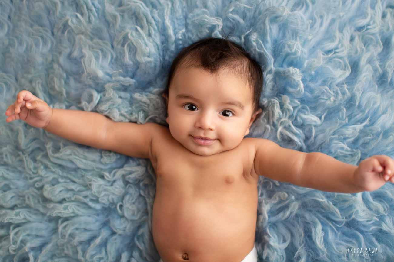 Charming baby boy photoshoot capturing the precious moments of a 6, 5, 4, 3-month-old on a soft blue rug against a serene blue backdrop. Expertly crafted by Anega Bawa, the renowned baby photographer in Delhi, Gurgaon, and Noida.