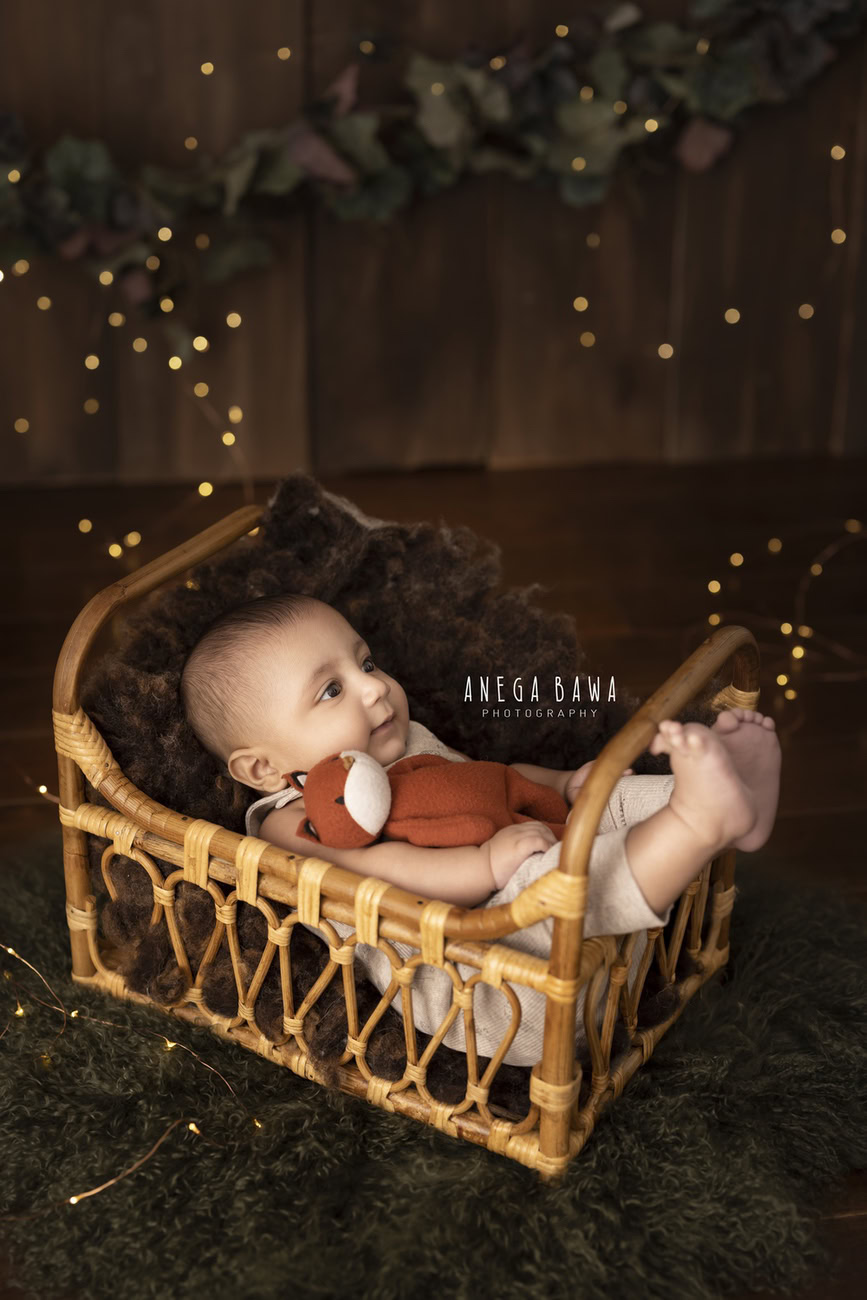 Create timeless memories of your baby boy's journey with a captivating photoshoot at 3, 4, 5, or 6 months. Featuring a rustic brown wooden cot adorned with golden lights, this enchanting setting captures the essence of innocence and warmth. Contact Anega Bawa for a magical experience in Delhi, Gurgaon, or Noida.