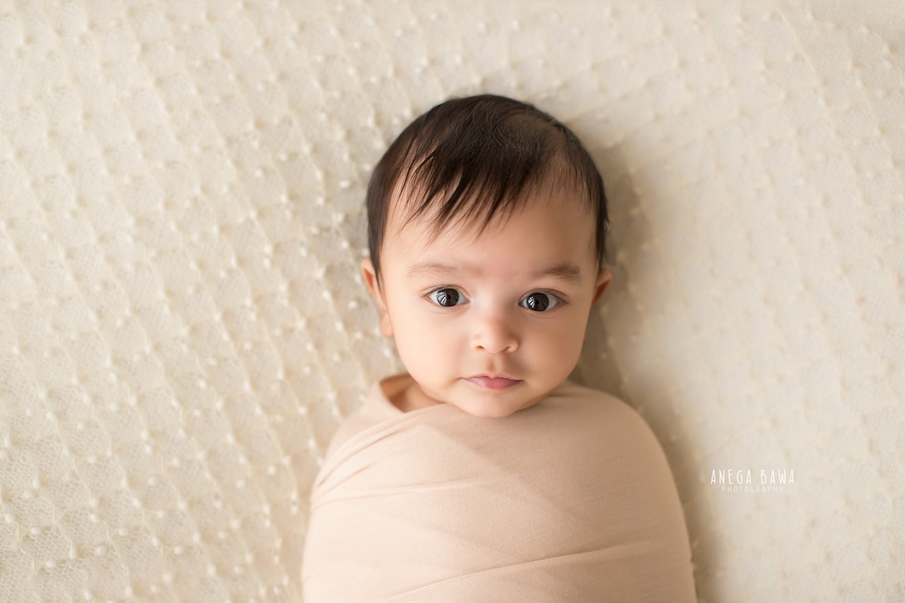 Captivating baby boy photoshoot showcasing the precious 6, 5, 4, 3-month-old wrapped in a cozy brown wrap against a pristine white backdrop. Crafted skillfully by Anega Bawa, the esteemed baby photographer in Delhi, Gurgaon, and Noida.