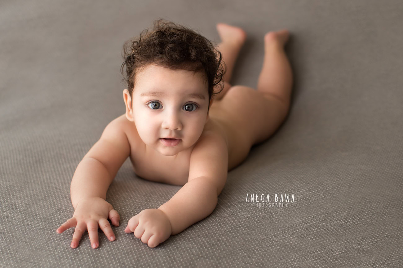 Charming baby boy photoshoot capturing the adorable 6, 5, 4, 3-month-old in a cute smiling pose against a sophisticated grey backdrop. Expertly crafted by Anega Bawa, the premier baby photographer in Delhi, Gurgaon, and Noida.