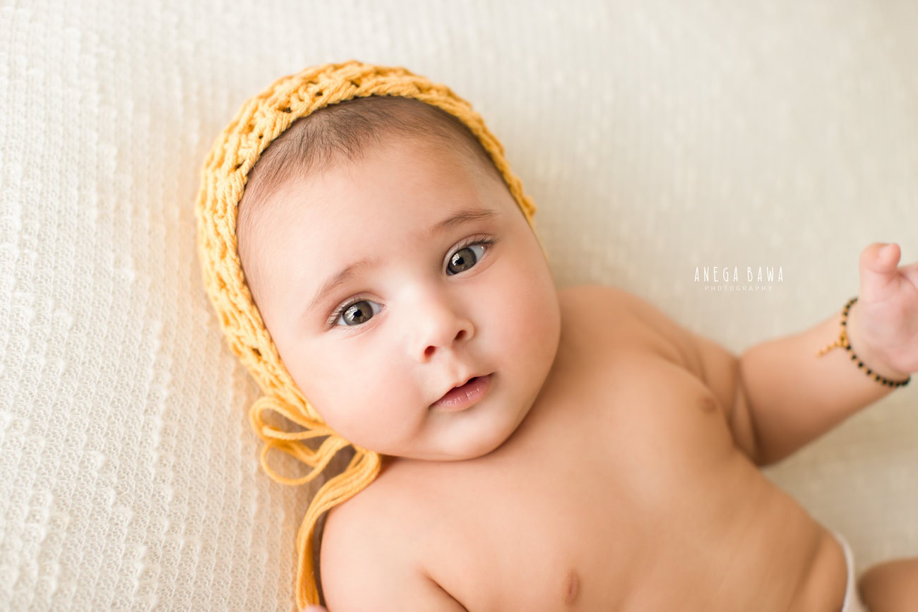 Capture the adorable moments of your baby boy's growth at 3, 4, 5, or 6 months with a charming yellow cap against a pristine white backdrop. Contact Anega Bawa for a delightful photoshoot experience in Delhi, Gurgaon, or Noida.