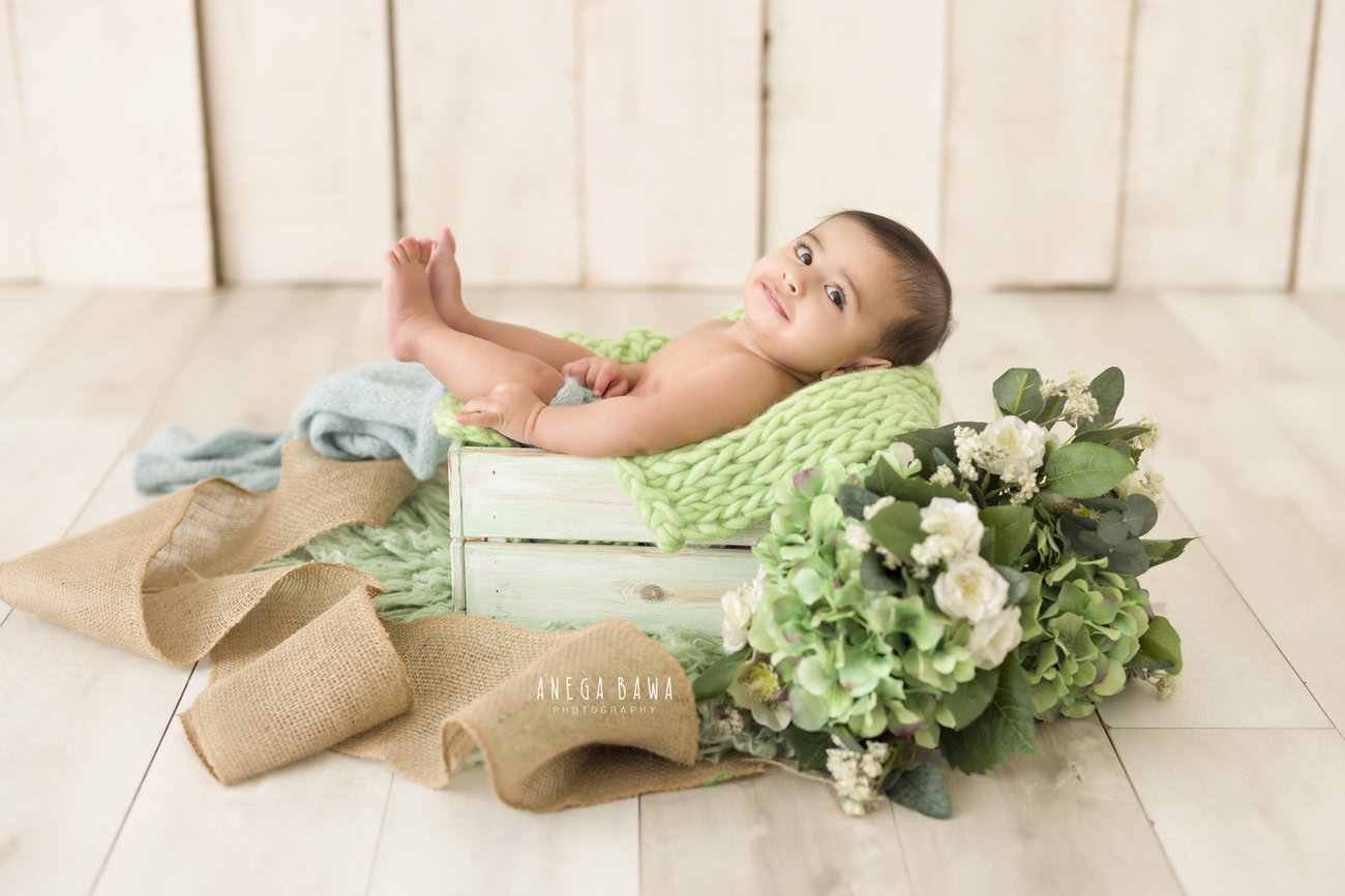 Baby boy photoshoot, 6, 5, 4, 3 months, green basket, beige backdrop, green leaves, white flowers. Location: Delhi, Gurgaon, Noida. Photographer: Anega Bawa.