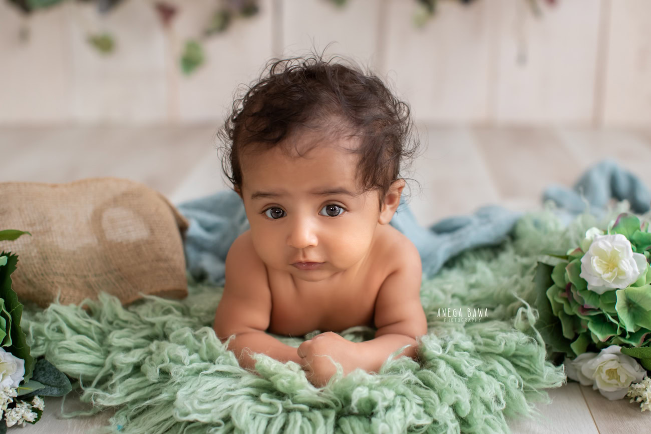 Enchanting baby boy photoshoot showcasing the adorable 6, 5, 4, 3-month-old on a vibrant green rug against a warm beige backdrop, adorned with a serene blue sheet. Crafted with expertise by Anega Bawa, the renowned baby photographer in Delhi, Gurgaon, and Noida.