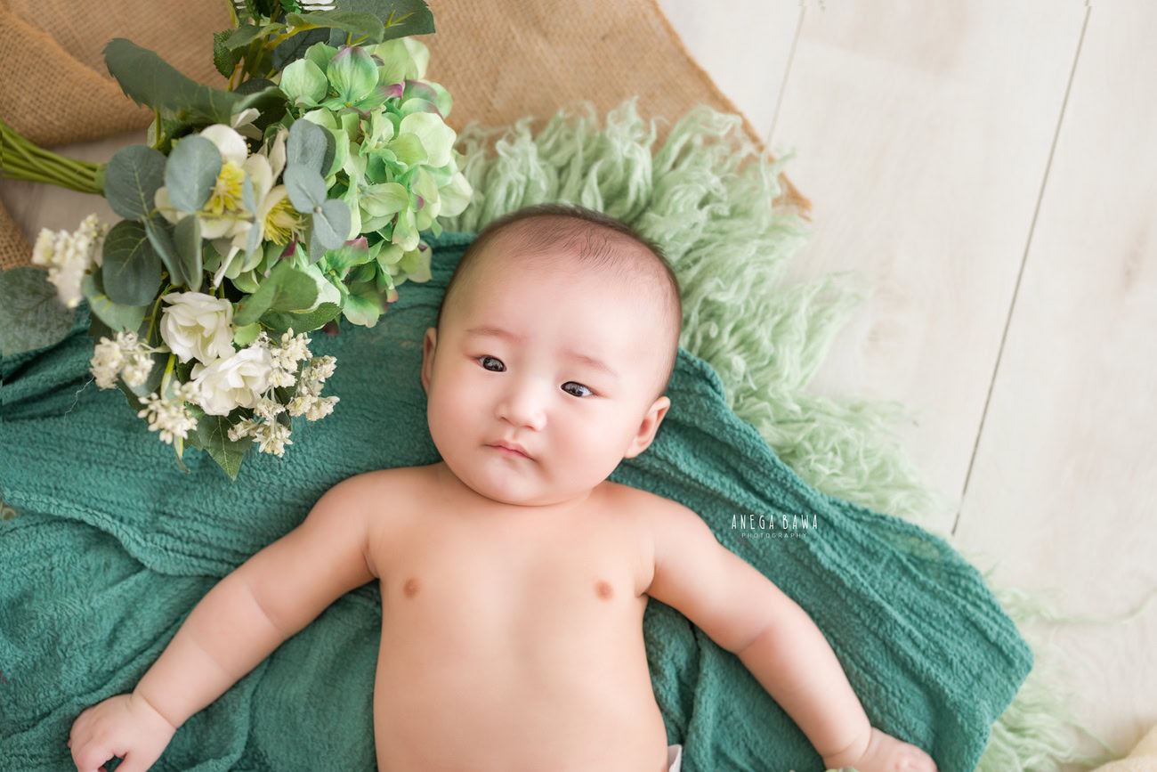 Baby boy photoshoot, 6, 5, 4, 3 months, green sheet, beige backdrop, floral curve. Location: Delhi, Gurgaon, Noida. Photographer: Anega Bawa.