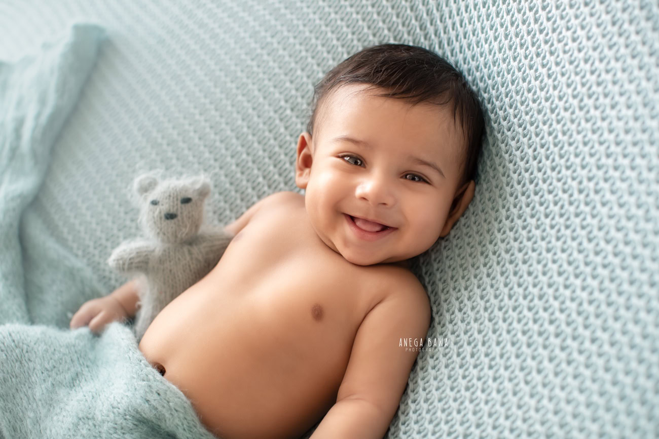 Captivating baby boy photoshoot featuring the endearing 6, 5, 4, 3-month-old against a sophisticated grey backdrop, wrapped in a serene blue wrap, accompanied by a charming soft toy. Crafted with expertise by Anega Bawa, the premier baby photographer in Delhi, Gurgaon, and Noida.