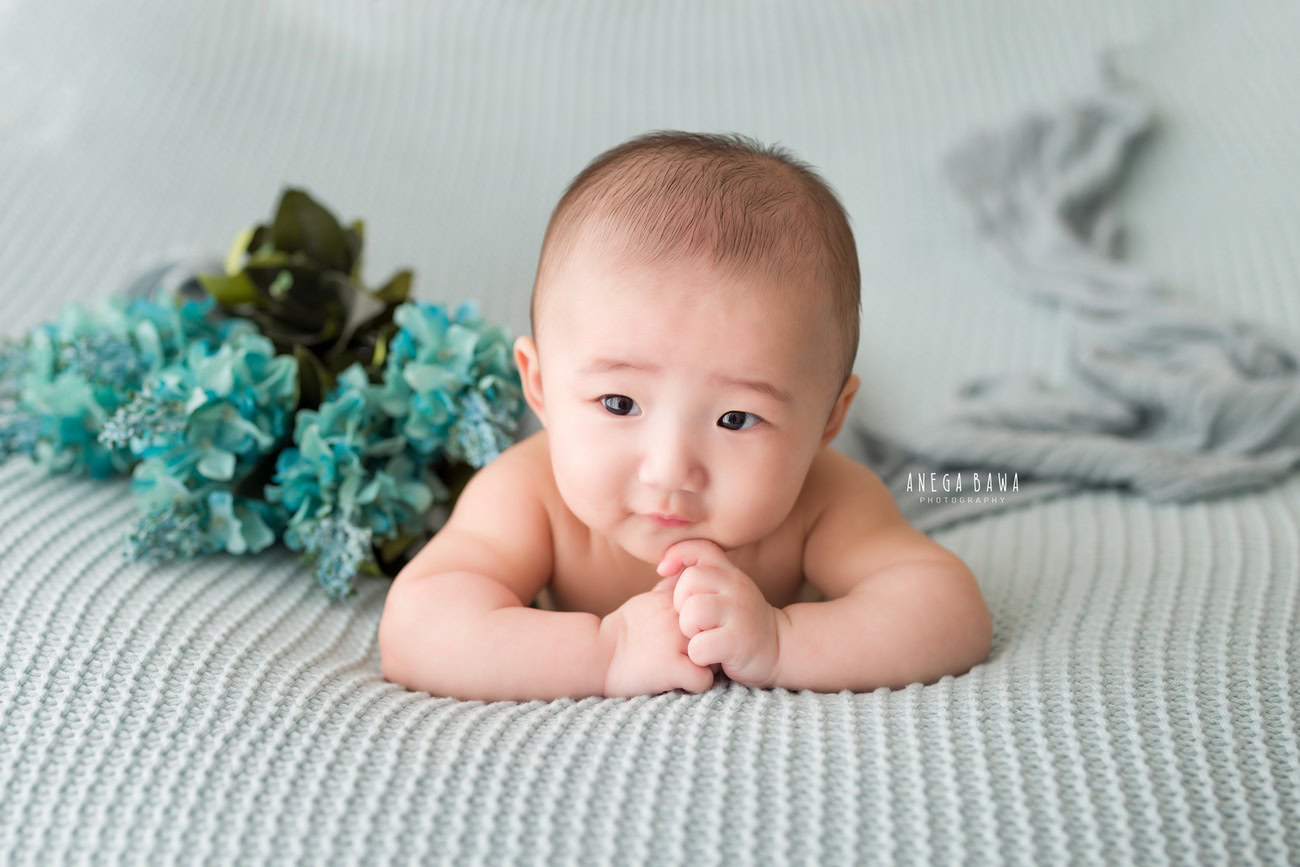 Baby boy photo shoot featuring a 6, 5, 4, or 3-month-old baby against a grey backdrop and sheet adorned with blue flowers, captured by photographer Anega Bawa in Delhi, Gurgaon, Noida