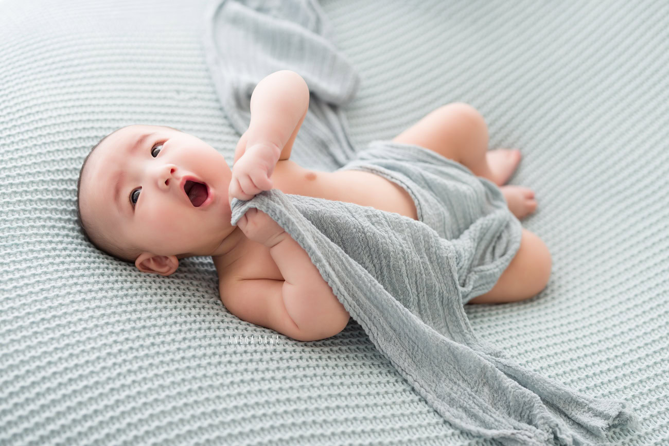 Baby boy photoshoot, 6 or 5 or 4 or 3 months, grey backdrop, grey wrap, cute smiling lying pose, Delhi Gurgaon Noida, Anega Bawa.