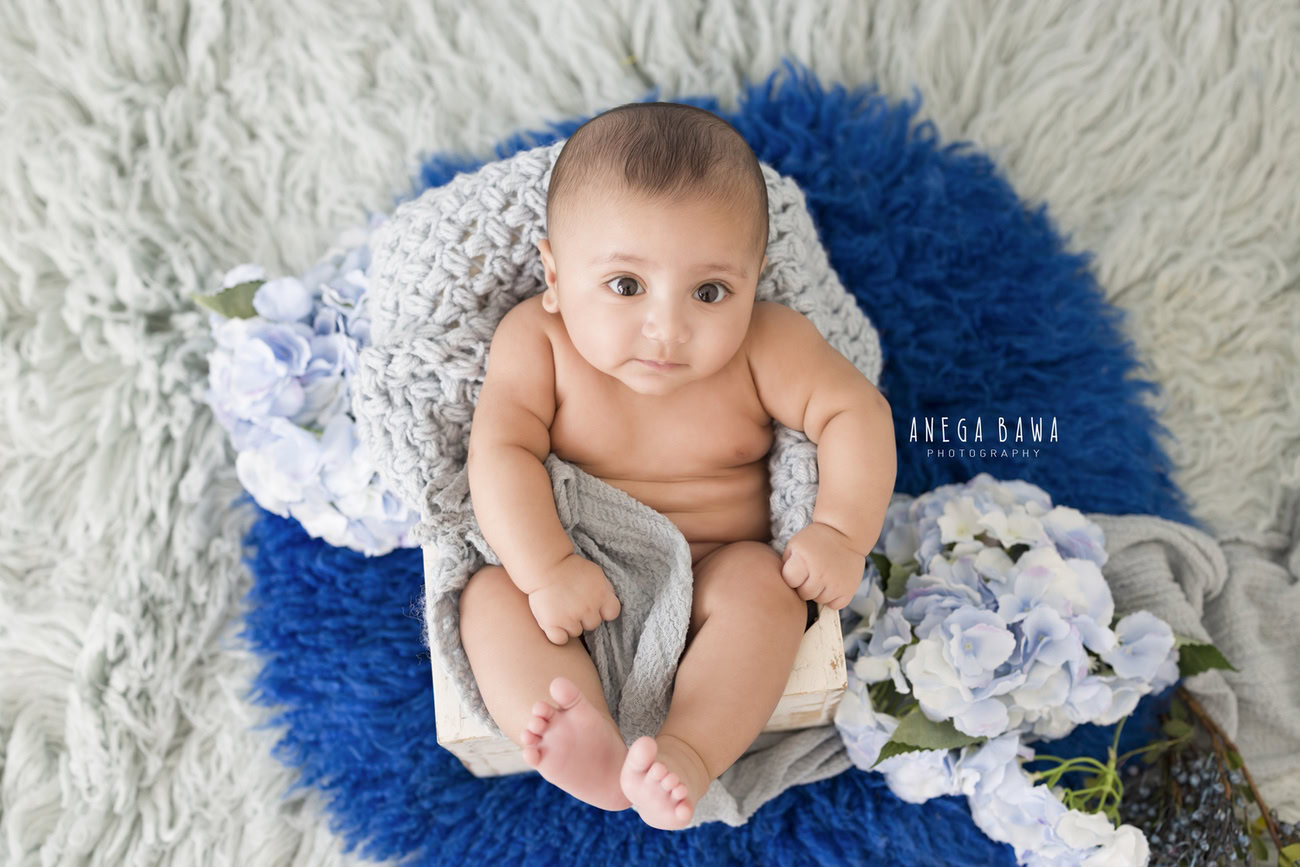 Capture the charm of your little one at 3, 4, 5, or 6 months with a grey rug and a snug grey wrap, surrounded by beautiful blue tulips. Contact Anega Bawa for baby boy photoshoots in Delhi, Gurgaon, or Noida.