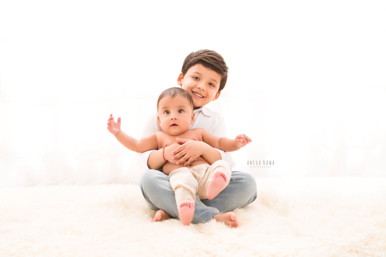 Capture the adorable moments of your baby boy aged 3, 4, 5, or 6 months on a white rug, along with siblings, against a serene white backdrop. Contact Anega Bawa for your photoshoot in Delhi, Gurgaon, or Noida.