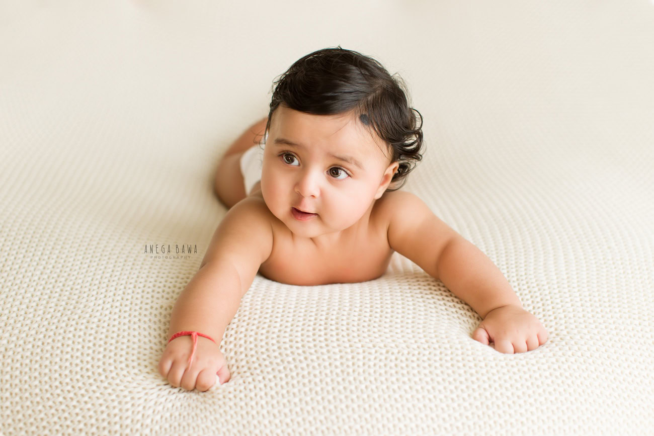 Enchanting baby boy photoshoot capturing the adorable 6, 5, 4, 3-month-old in a cute lying pose on a pristine white sheet. Skillfully crafted by Anega Bawa, the premier baby photographer in Delhi, Gurgaon, and Noida.