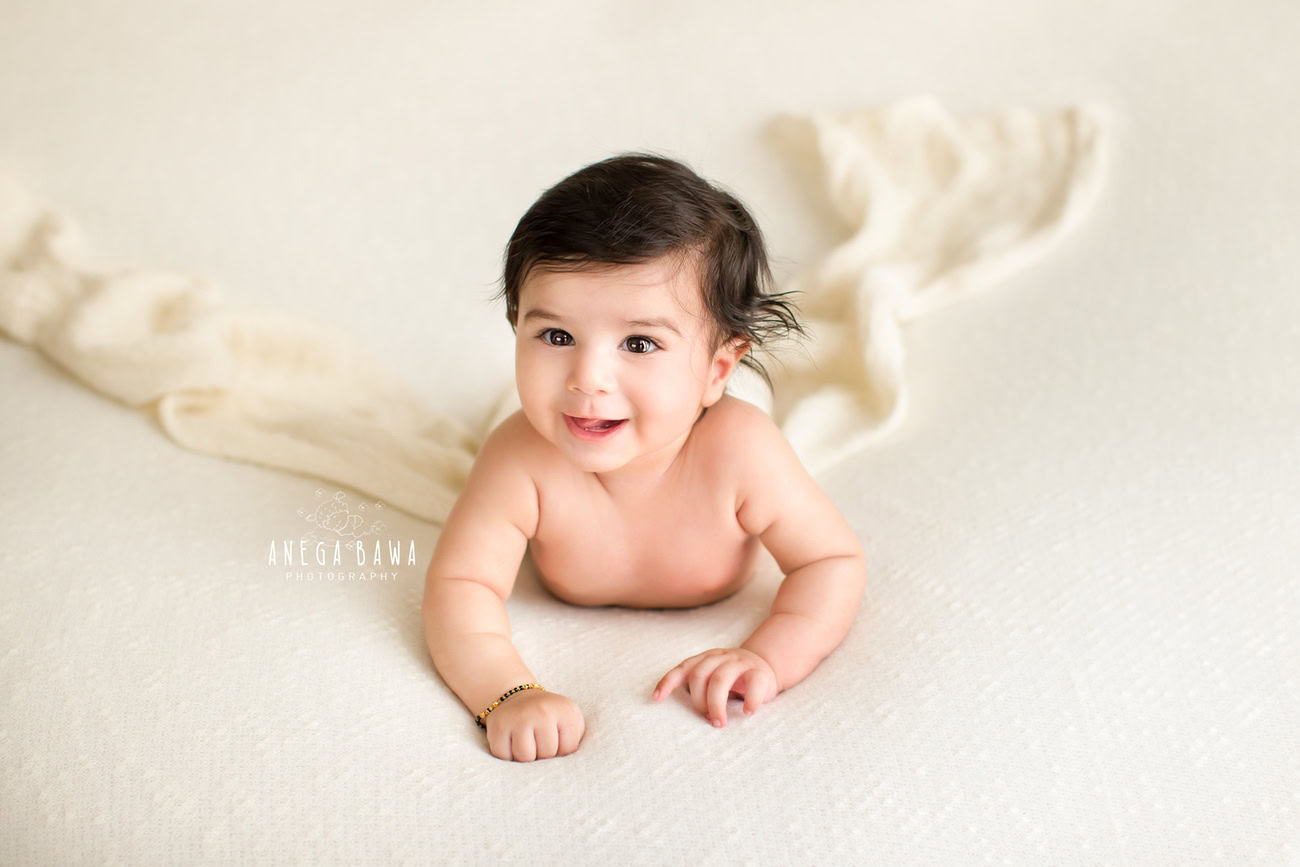 Captivating baby boy photoshoot showcasing the innocence of a 6, 5, 4, 3-month-old on a pristine white sheet against a pure white backdrop. Skillfully captured by Anega Bawa, the esteemed baby photographer in Delhi, Gurgaon, and Noida.