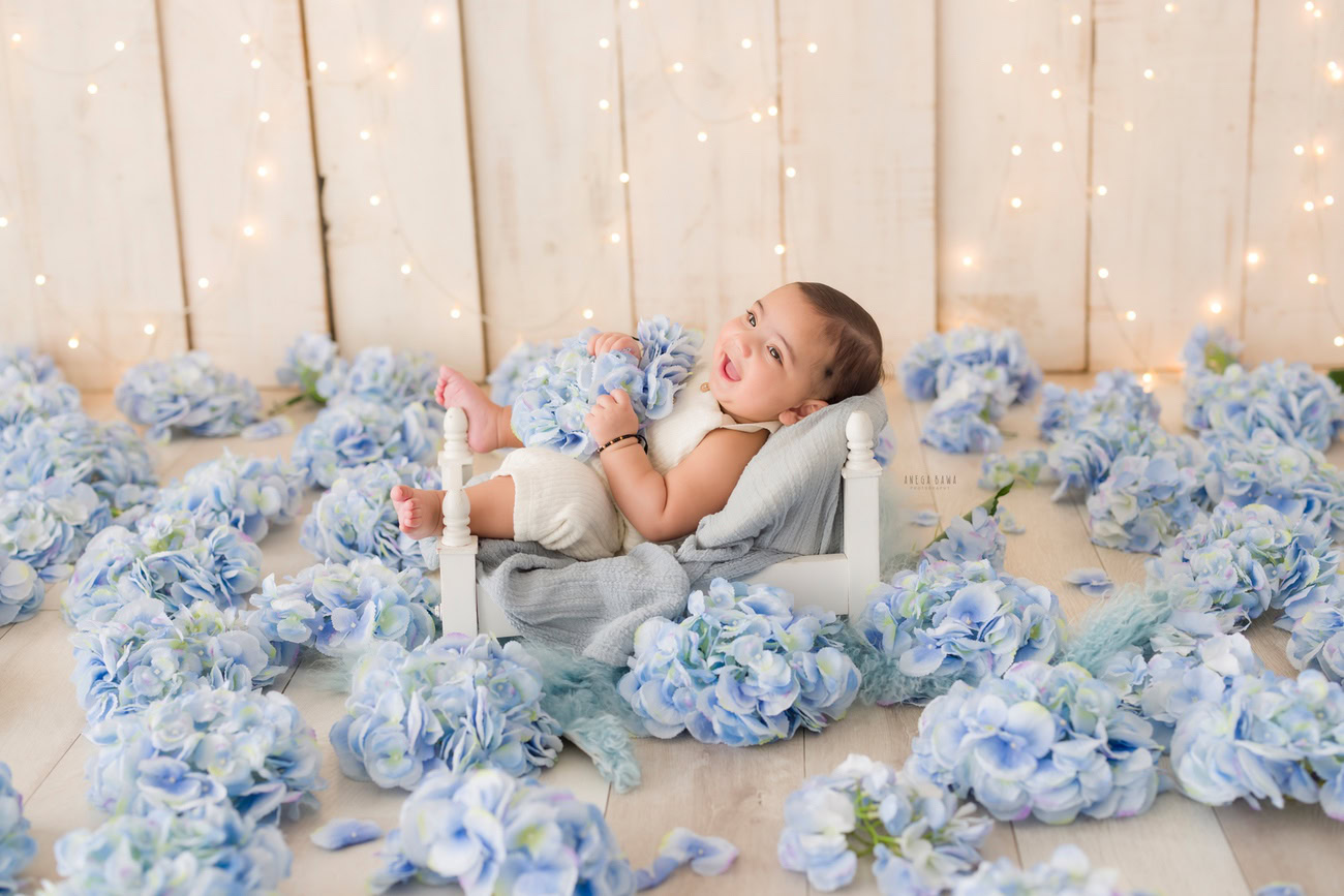 Baby boy photoshoot, 6 or 5 or 4 or 3 months, white wooden cot, blue flowers, beige backdrop, golden lights. Location: Delhi, Gurgaon, Noida. Photographer: Anega Bawa.