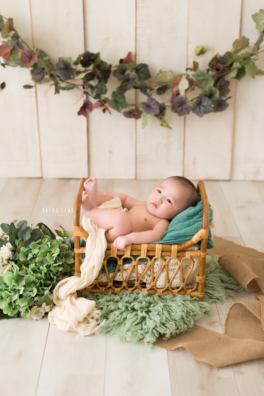 Baby boy photoshoot, 6 or 5 or 4 or 3 months, wooden cot, beige sheet, beige backdrop, green leafy curve. Location: Delhi, Gurgaon, Noida. Photographer: Anega Bawa.