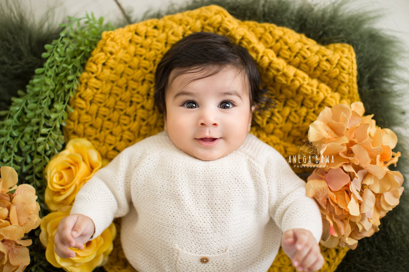 Captivating baby boy photoshoot showcasing the charming 6, 5, 4, 3-month-old in a stylish white baby boysuit against a vibrant yellow and green backdrop. Skillfully captured by Anega Bawa, the esteemed baby photographer in Delhi, Gurgaon, and Noida.