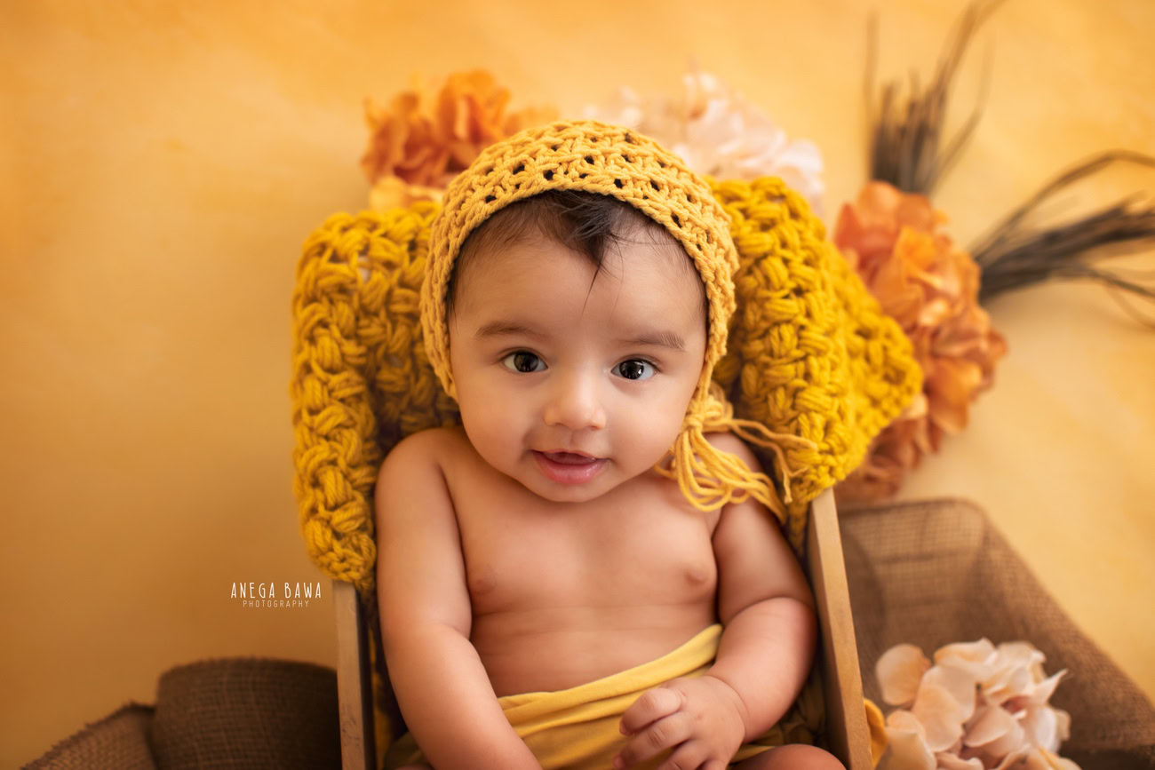 Captivating baby boy photoshoot showcasing the charming 6, 5, 4, 3-month-old adorned with a sunny yellow cap, against a vibrant yellow backdrop, wrapped in a matching yellow wrap. Skillfully crafted by Anega Bawa, the premier baby photographer in Delhi, Gurgaon, and Noida.