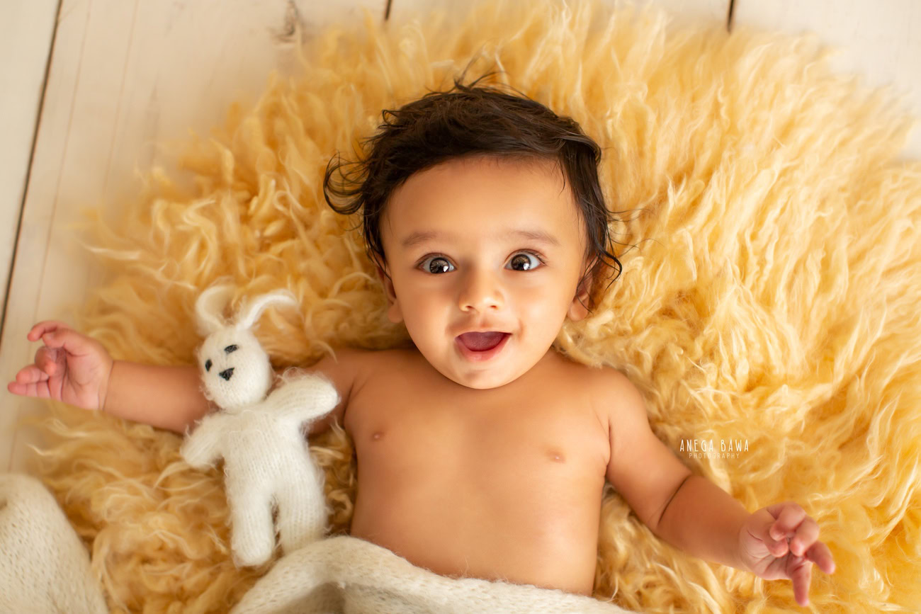 Captivating baby boy photoshoot featuring the delightful 6, 5, 4, 3-month-old on a cozy yellow rug accompanied by a cuddly soft toy against a warm beige backdrop. Skillfully captured by Anega Bawa, the esteemed baby photographer in Delhi, Gurgaon, and Noida.