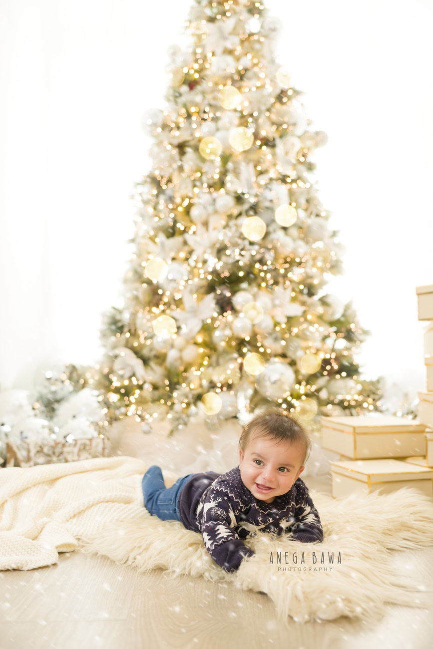 Embrace the festive cheer with your little one aged 3, 4, 5, or 6 months in a charming Xmas jumper, surrounded by the glow of a decorated Xmas tree and golden lights, against a pristine white backdrop, nestled on a cozy beige rug. Reach out to Anega Bawa for captivating baby boy photoshoots in Delhi, Gurgaon, or Noida.