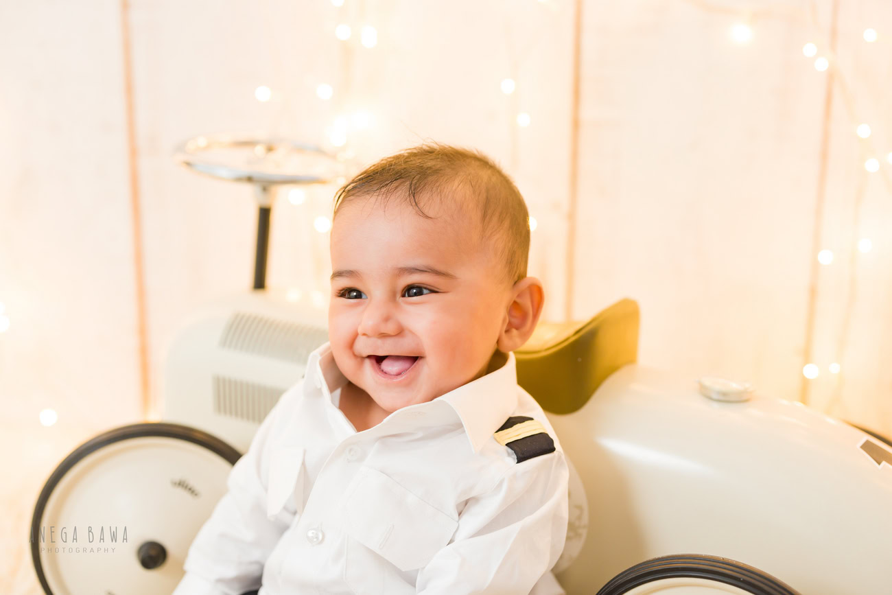 Baby boy photoshoot ideas, 5 or 4 or 3 or 6 months, beige backdrop, white shirt, naughty smiling pose. Location: Delhi, Gurgaon, Noida. Photographer: Anega Bawa.