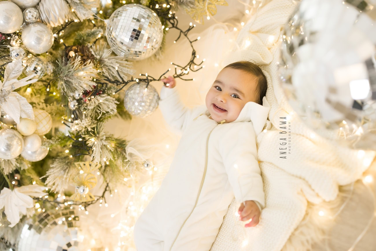 Create unforgettable memories with your baby boy aged 3, 4, 5, or 6 months in a charming white baby boysuit, surrounded by twinkling discoballs against a warm beige backdrop. Contact Anega Bawa for captivating baby boy photoshoots in Delhi, Gurgaon, or Noida.
