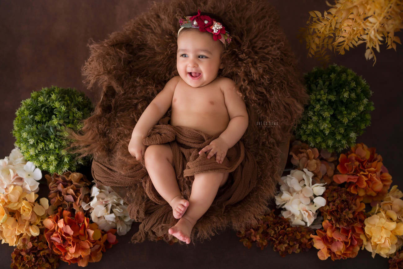 Baby girl photo shoot, 6 or 5 or 3 or 4 months, brown rug, brown backdrop, orange yellow flowers. Location: Delhi, Gurgaon, Noida. Photographer: Anega Bawa.