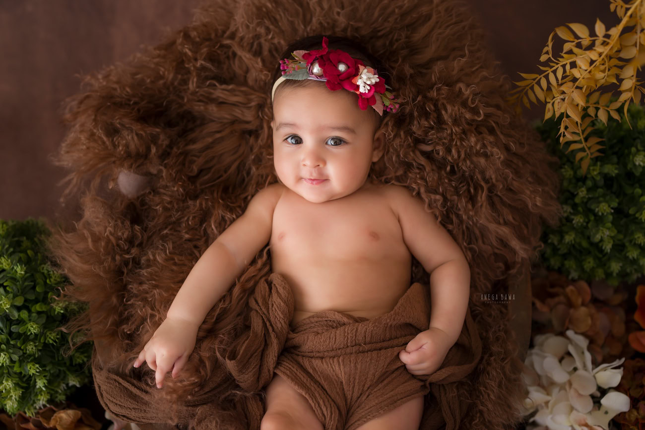 Baby girl photo shoot featuring a brown wrap and brown rug, adorned with a cute headband. The shoot was conducted by Anega Bawa in Delhi, Gurgaon, Noida for babies aged 6, 5, 3, or 4 months.