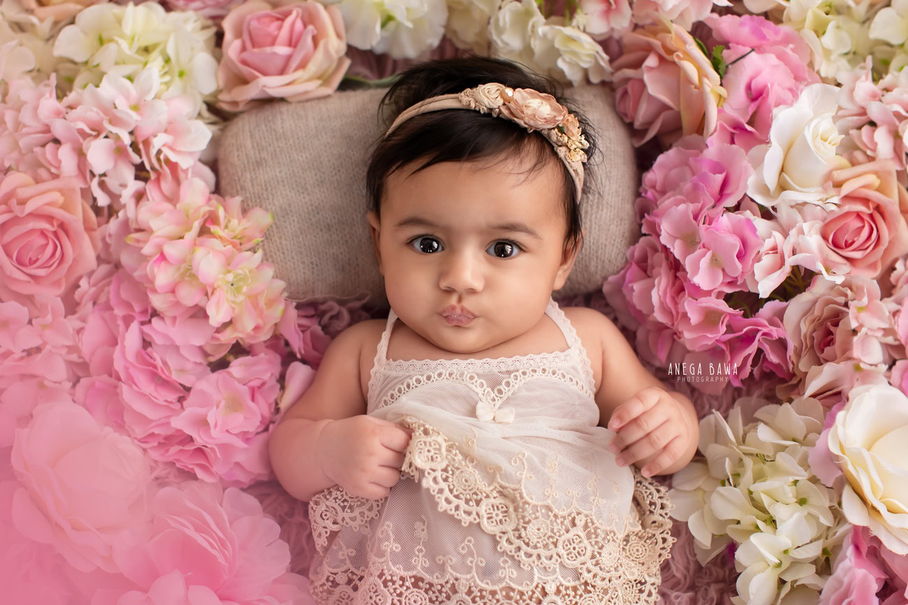 Captivating baby girl photoshoot showcasing the adorable 6, 5, 3, 4-month-old against a vibrant floral backdrop, adorned with a cute headband, striking a pout pose. Skillfully crafted by Anega Bawa, the premier baby photographer in Delhi, Gurgaon, and Noida.