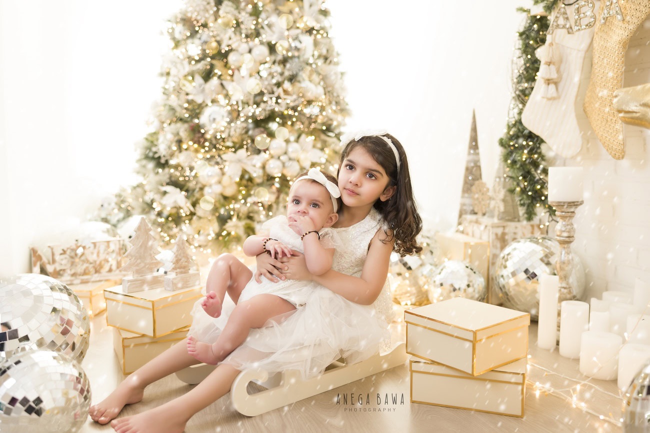 Capture the sweetness of your baby girl and her sibling aged 3, 4, or 5 months in a heartwarming photoshoot featuring a festive setup with a Christmas tree and disco balls against a clean white backdrop. Contact Anega Bawa for memorable baby girl photo sessions in Delhi, Gurgaon, or Noida.