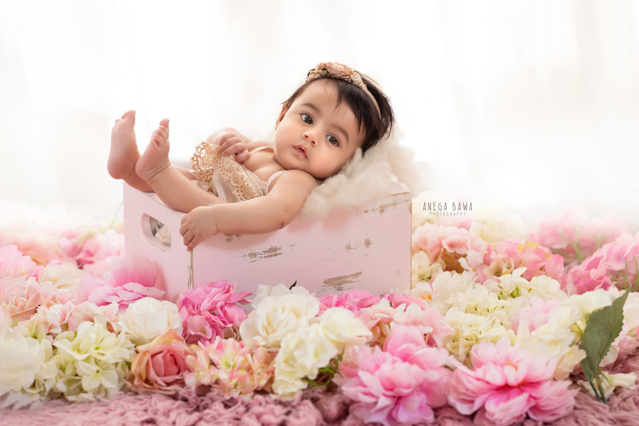 Captivating baby girl photoshoot featuring the adorable 6, 5, 3, 4-month-old against a pristine white backdrop, nestled in a charming pink basket adorned with a cute headband. Skillfully crafted by Anega Bawa, the premier baby photographer in Delhi, Gurgaon, and Noida.