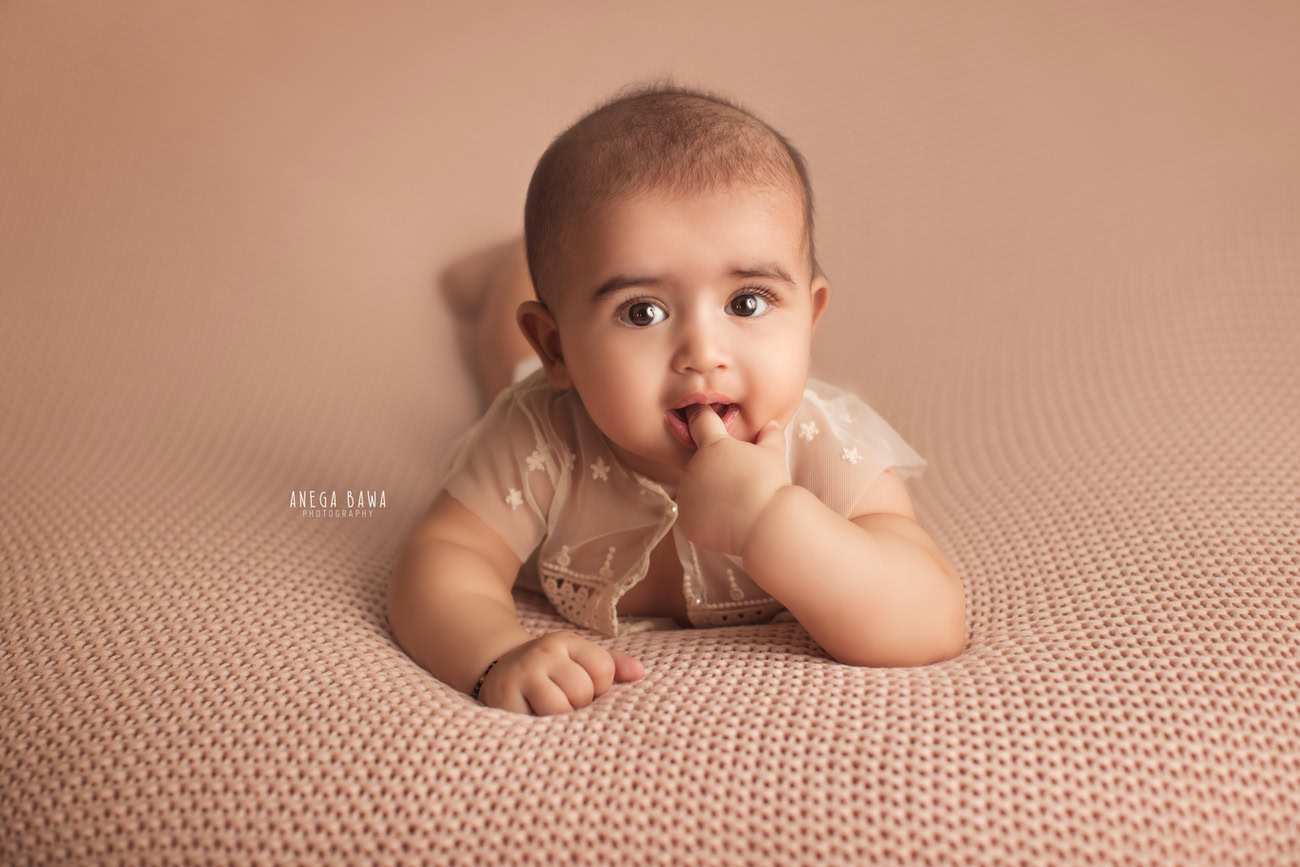 Captivating baby girl photoshoot featuring the charming 6, 5, 4, 3-month-old in a cute lying down pose against a rich brown backdrop. Skillfully crafted by Anega Bawa, the premier baby photographer in Delhi, Gurgaon, and Noida.