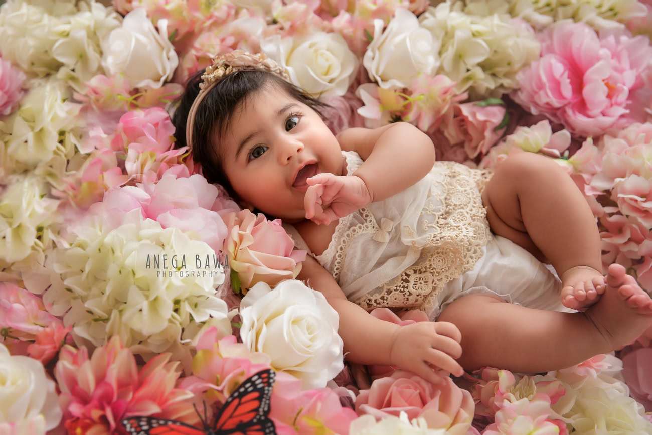 Captivating baby girl photoshoot capturing the adorable 6, 5, 4, 3-month-old in a cute lying pose surrounded by flowers on the floor. Skillfully crafted by Anega Bawa, the premier baby photographer in Delhi, Gurgaon, and Noida.