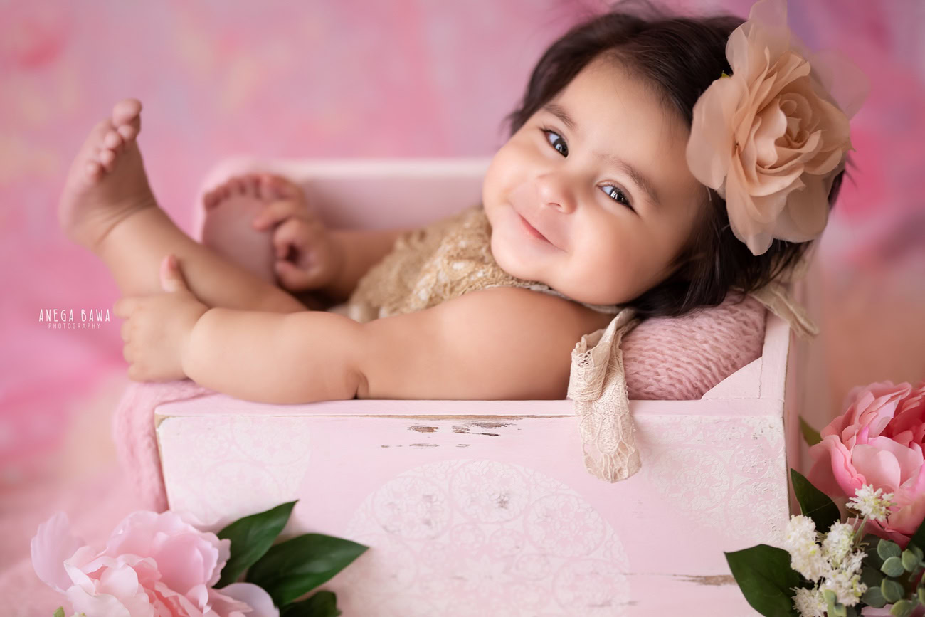 Captivating baby girl photoshoot featuring the adorable 6, 5, 4, 3-month-old nestled in a charming pink basket, adorned with a cute flower as a headband, against a soft pink backdrop. Skillfully crafted by Anega Bawa, the premier baby photographer in Delhi, Gurgaon, and Noida.