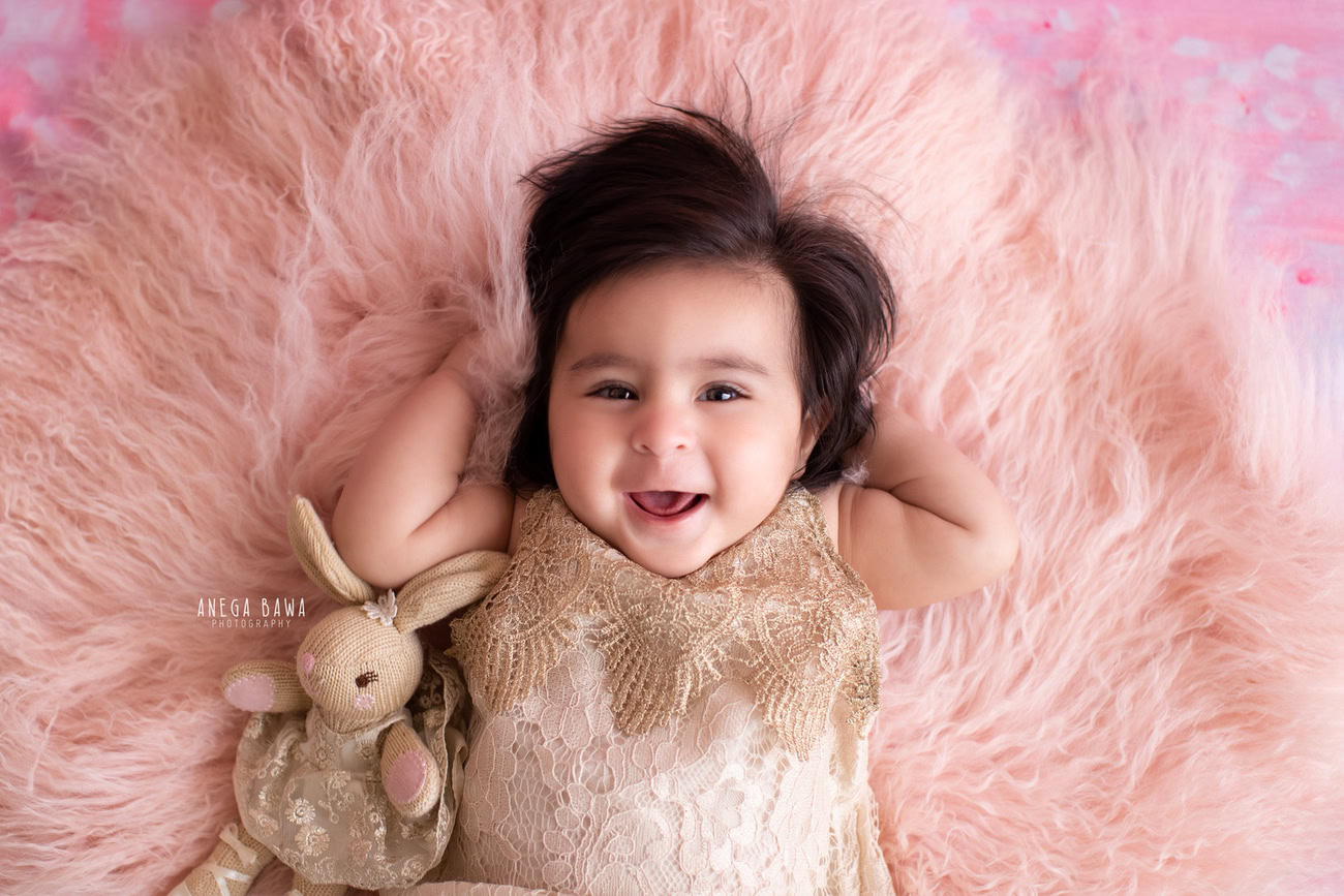 Captivating baby girl photoshoot showcasing the enchanting 6, 5, 4, 3-month-old on a soft pink rug, adorned in a golden dress and accompanied by a cuddly soft toy, against a charming pink backdrop. Skillfully crafted by Anega Bawa, the premier baby photographer in Delhi, Gurgaon, and Noida.
