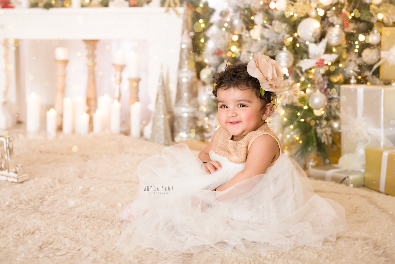 Capture the precious moments of your baby girl's growth journey at 3, 4, 5, or 6 months with a charming photoshoot featuring a beige rug, accessorized with a cute flower as a hair accessory, set against a backdrop of a Christmas tree. Contact Anega Bawa, the expert baby girl photographer in Delhi, Gurgaon, or Noida, for timeless memories.