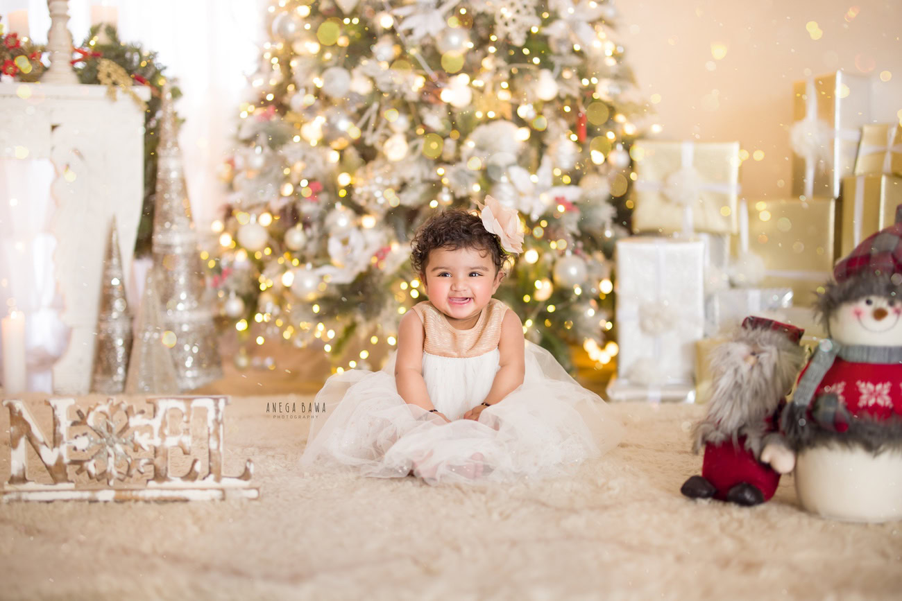 Capture the timeless charm of your baby girl at 3, 4, 5, or 6 months with a captivating photoshoot featuring a beige rug, adorned with a Christmas tree and golden lights, against a beige backdrop. Cherish the sweet moments as your little one strikes a cute seating pose. Contact Anega Bawa, the expert baby girl photographer in Delhi, Gurgaon, or Noida, to preserve these precious memories.