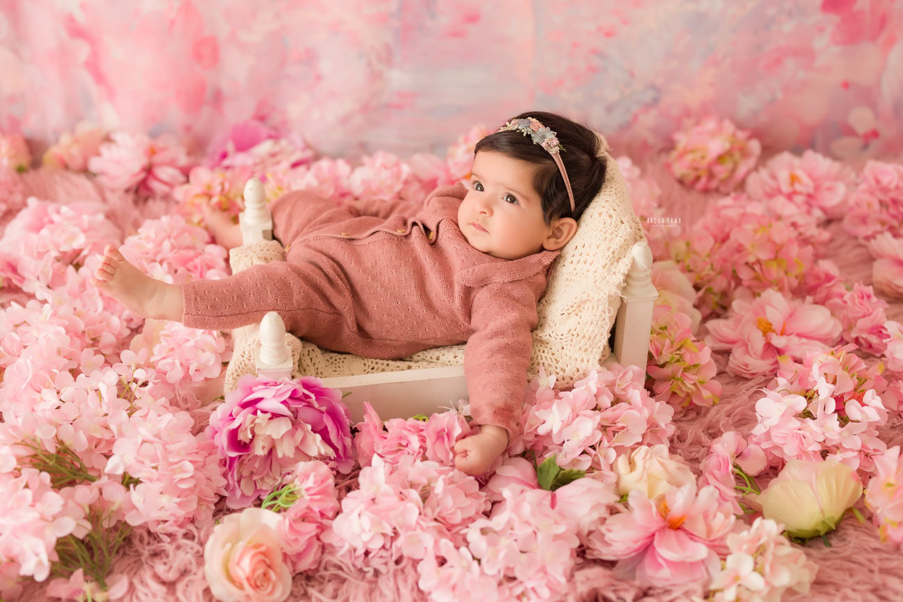 Baby girl photographer, 3 or 4 or 5 or 6 months, peach baby suit, pink backdrop, flowers on floor. Location: Delhi, Gurgaon, Noida. Photographer: Anega Bawa.