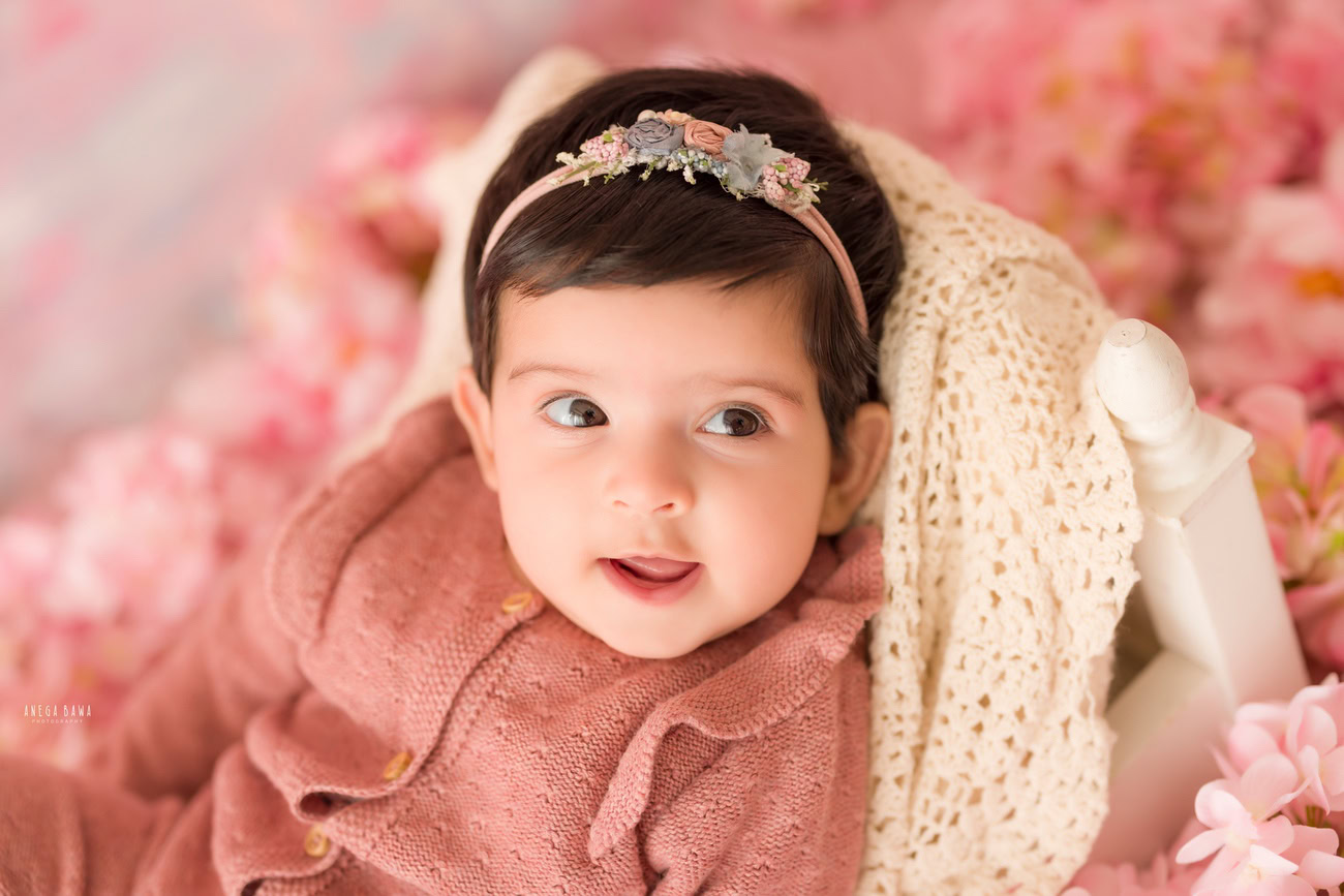 Baby girl photographer, 3 or 4 or 5 or 6 months, peach baby suit, pink flower backdrop, cute headband. Location: Delhi, Gurgaon, Noida. Photographer: Anega Bawa.