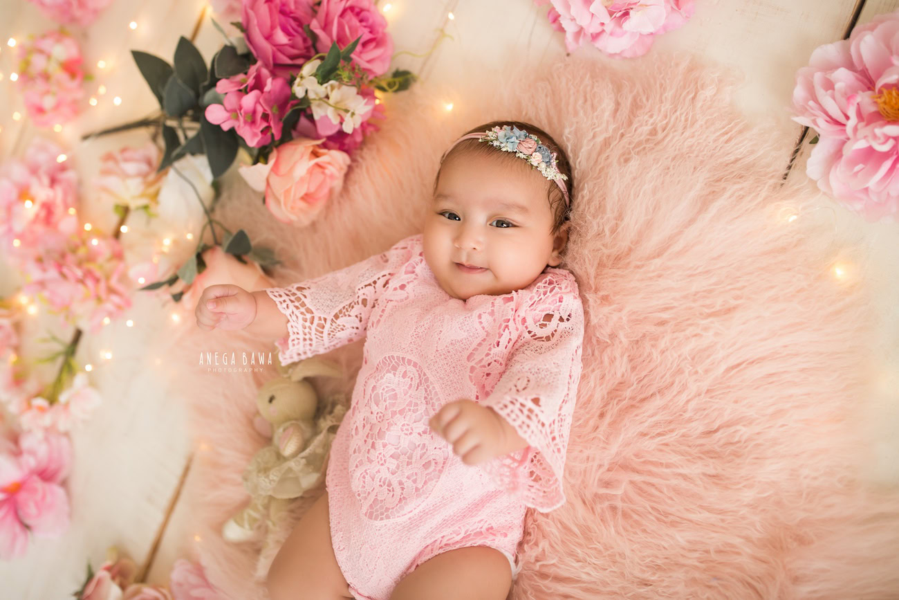 Experience the sweetness of your baby girl's milestones at 3, 4, 5, or 6 months with a delightful photoshoot featuring a pink babysuit, peach and pink flowers, and a soft toy against a peach backdrop. Reach out to Anega Bawa, the renowned baby girl photographer in Delhi, Gurgaon, or Noida, to capture these precious moments.