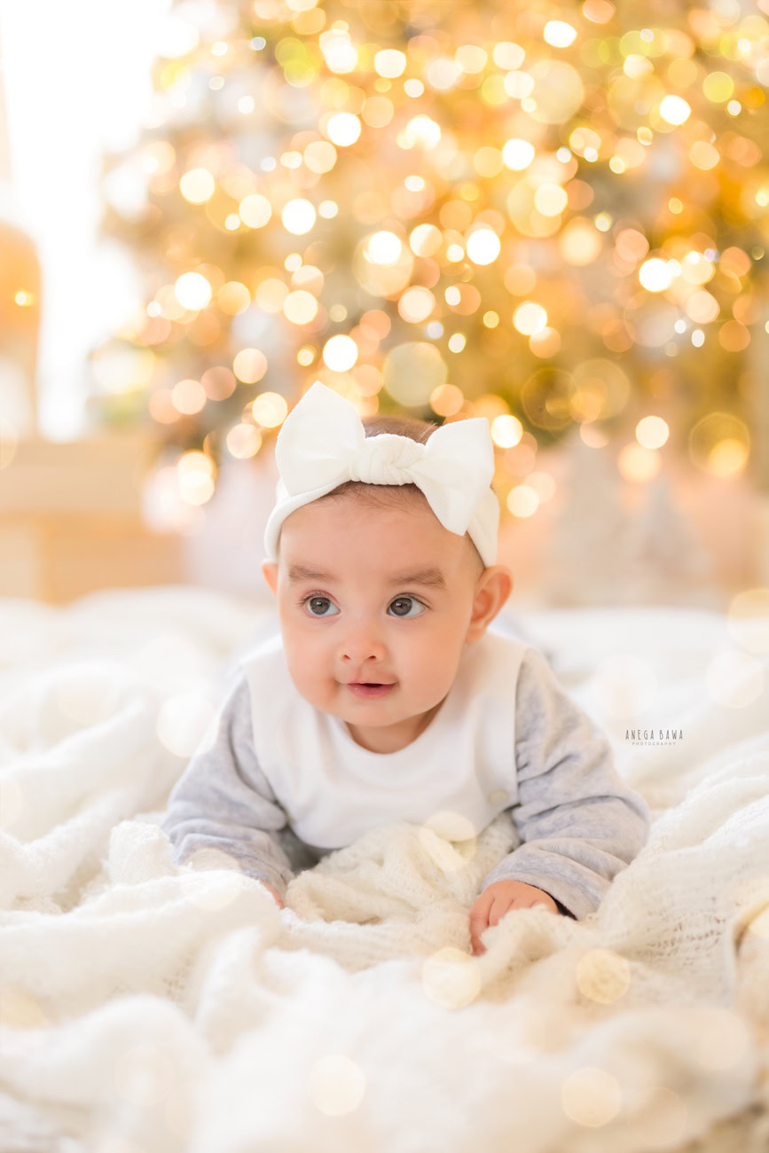 Baby girl photographer, 3, 4, 5, or 6 months, Christmas tree, cute seating pose. Location: Delhi, Gurgaon, Noida. Photographer: Anega Bawa.