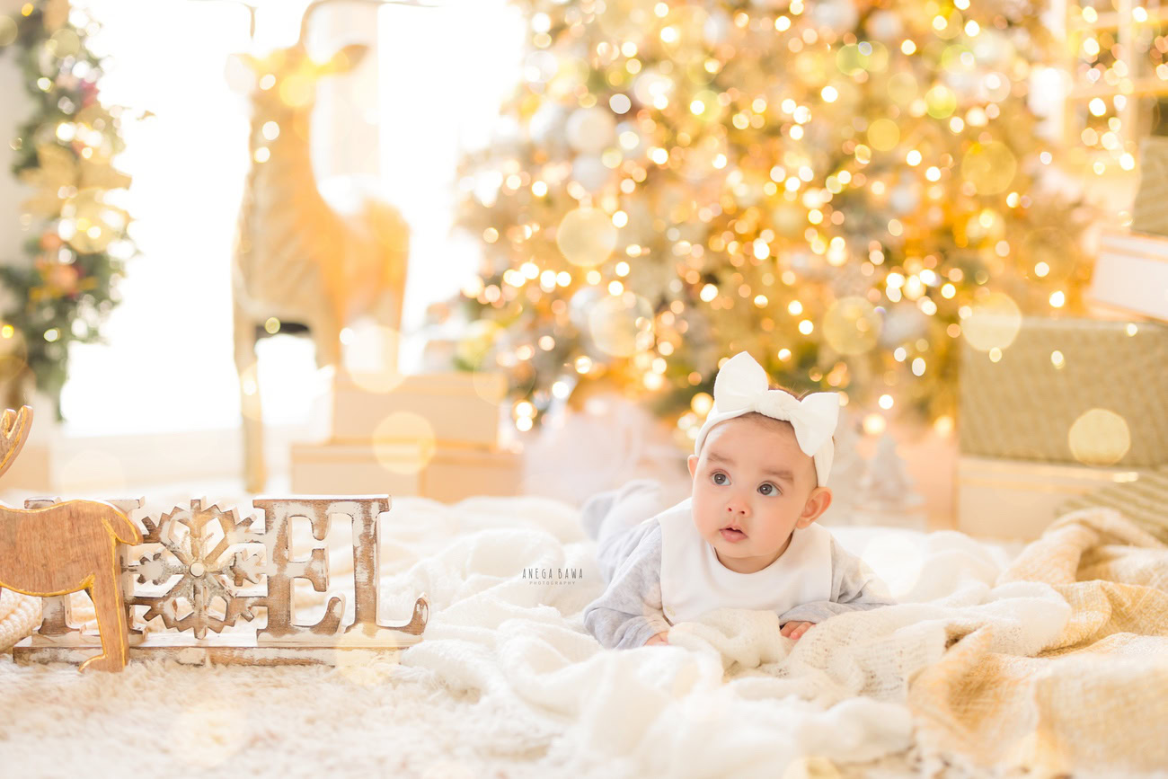 Baby girl photographer, 3, 4, 5, or 6 months, Christmas tree, golden lights, cute white headband. Location: Delhi, Gurgaon, Noida. Photographer: Anega Bawa.