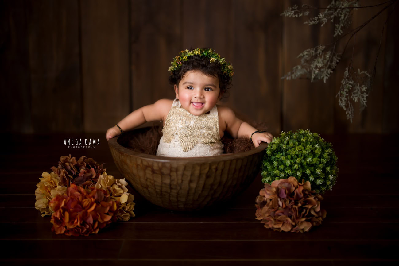 Capture the precious moments of your baby girl's journey at 3, 4, or 5 months with a delightful brown-themed photoshoot. Adorned with a cute headband, she'll be nestled in a charming brown basket amidst green and brown flowers, all set against a complementary brown backdrop. Contact Anega Bawa for exquisite baby girl photography in Delhi, Gurgaon, or Noida.