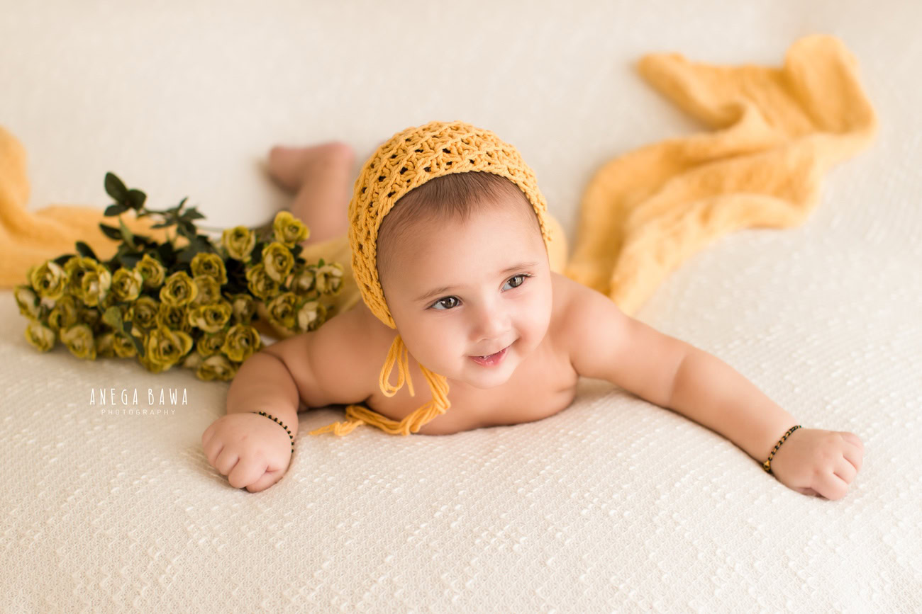 Celebrate the innocence of your baby girl at 3, 4, or 5 months with a charming photography session. Adorned in a cute yellow cap, she'll be surrounded by vibrant green flowers against a pristine white backdrop. Contact Anega Bawa for exquisite baby girl photography in Delhi, Gurgaon, or Noida.