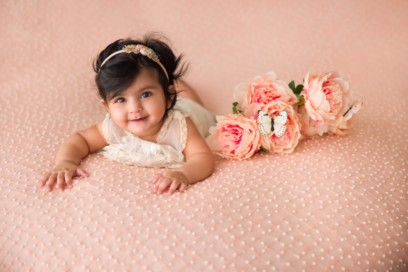 Capture the sweetness of your 4 to 6-month-old baby girl with a delightful peach backdrop complemented by peach flowers, in a serene lying-down pose. Contact Anega Bawa for professional baby girl photography in Delhi, Gurgaon, or Noida.