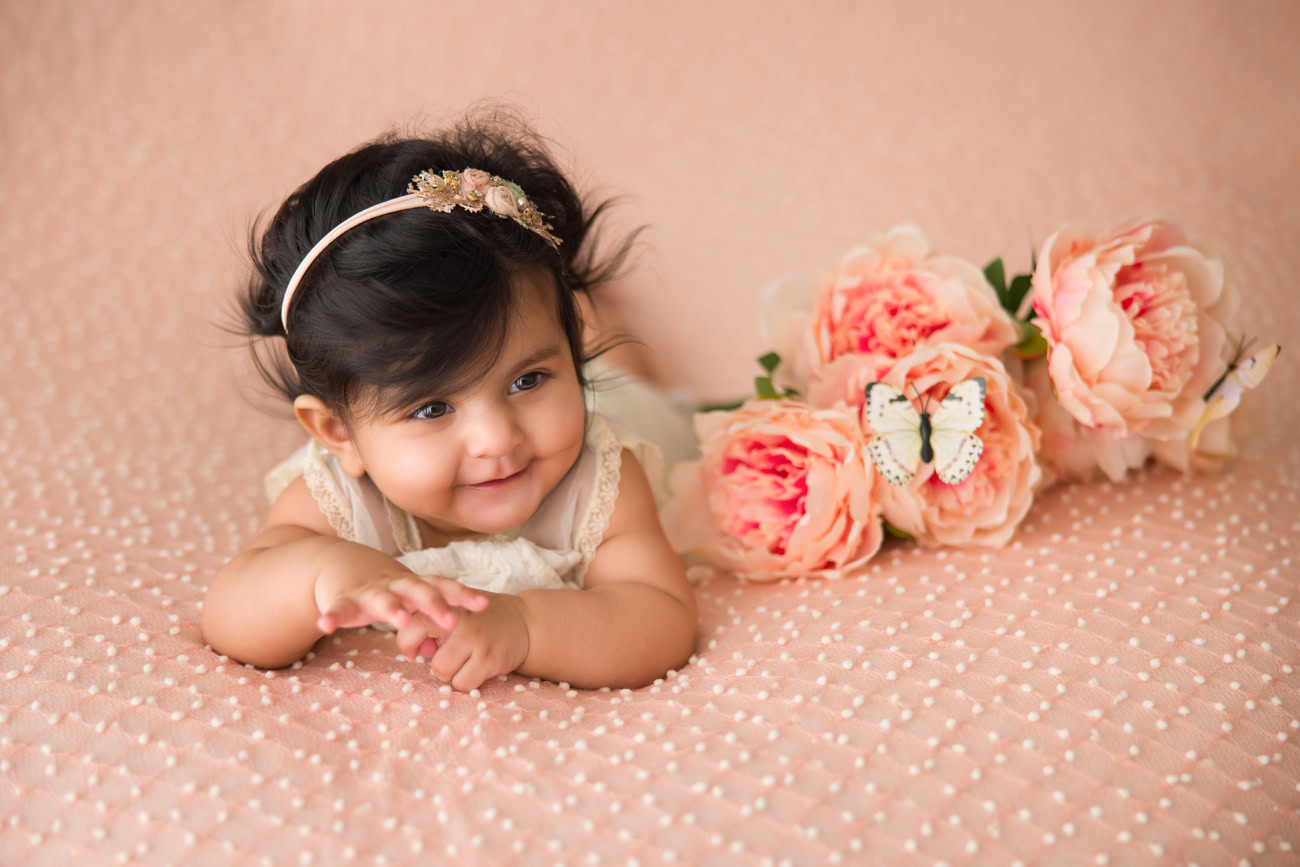 Baby girl photography session for 3, 4, and 5-month-olds featuring a lovely peach backdrop adorned with peach flowers. Contact Anega Bawa for booking in Delhi, Gurgaon, or Noida.