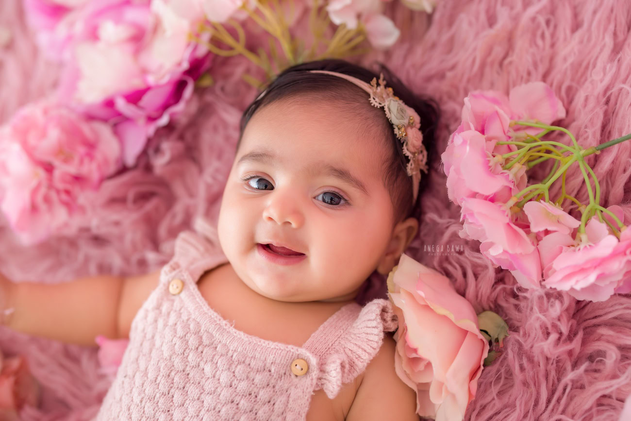 Delight in the sweetness of your baby girl's milestones with a charming pink backdrop and rug, captured by Anega Bawa in Delhi, Gurgaon, or Noida.