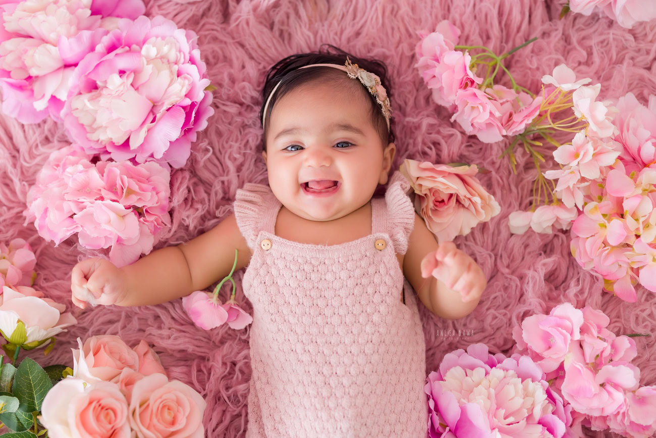 Embrace the innocence of your little one with a pink dress, complemented by a soft rug and a cute headband, in a photoshoot by Anega Bawa in Delhi, Gurgaon, or Noida.
