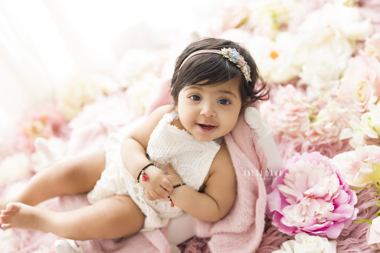 Capture the sweetness of your baby girl amidst pink flowers and a floral backdrop, adorned with a cute headband, courtesy of Anega Bawa's photography in Delhi, Gurgaon, or Noida.