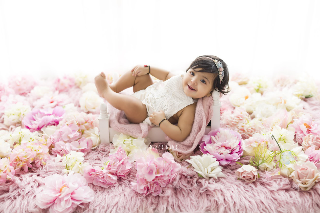 Create everlasting memories of your baby girl surrounded by pink and white flowers on a soft pink rug against a white backdrop. Schedule a photoshoot with Anega Bawa in Delhi, Gurgaon, or Noida.